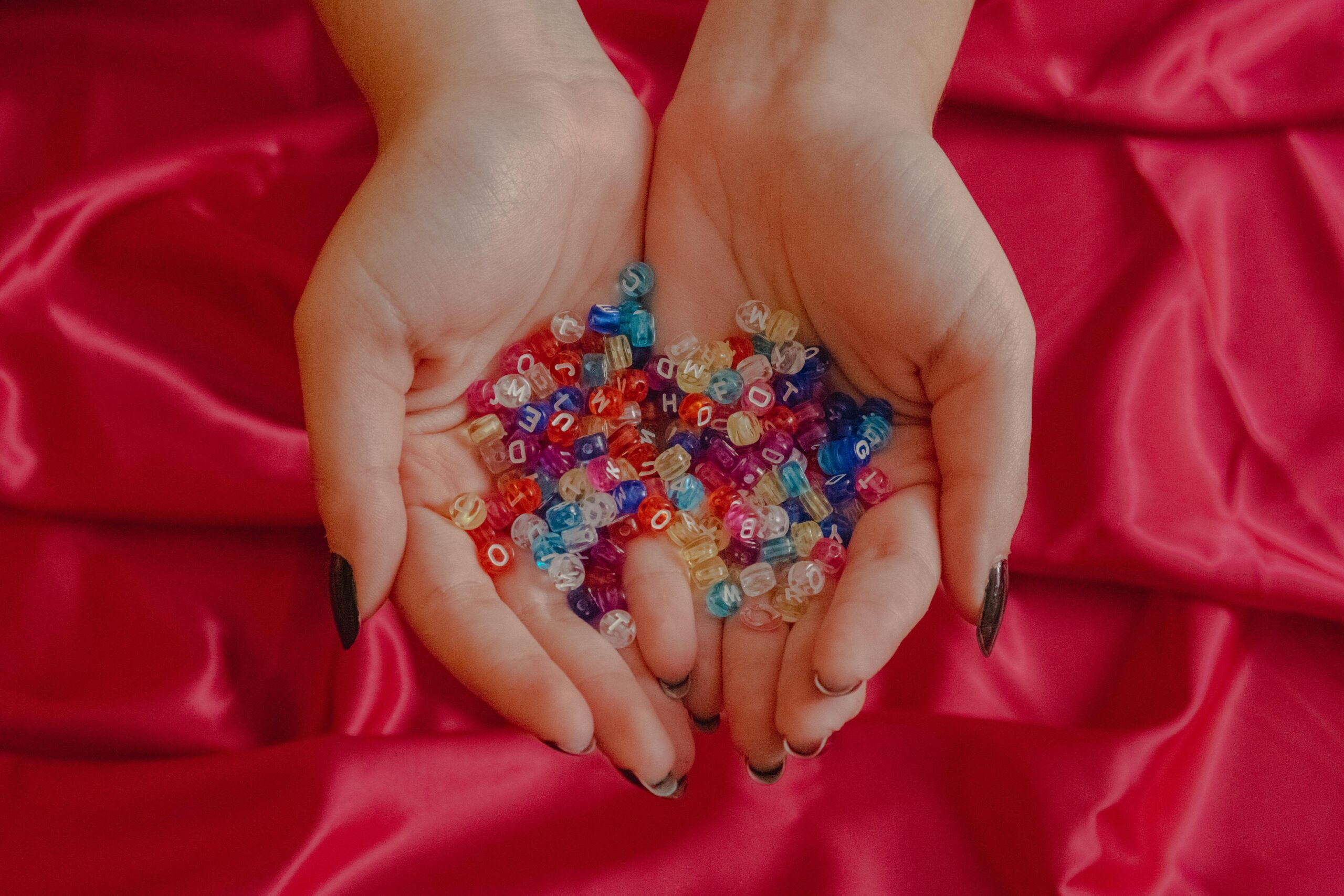 Close-up of hands holding colorful letter beads against a vibrant red silk background.